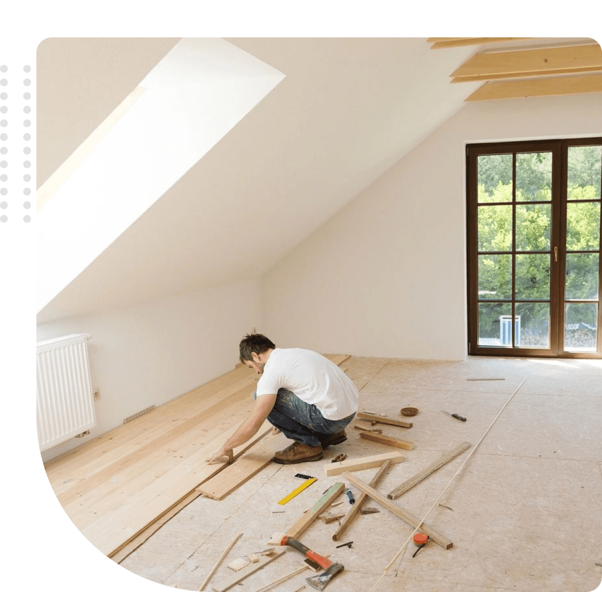 Man installing wooden flooring in a bright attic room.