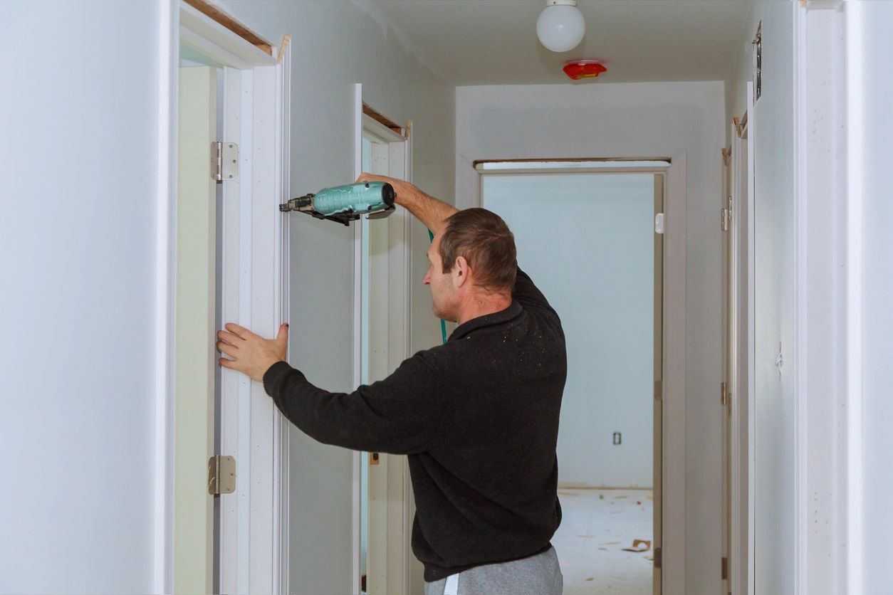 Man measuring doorframe width with a tape measure inside a home.