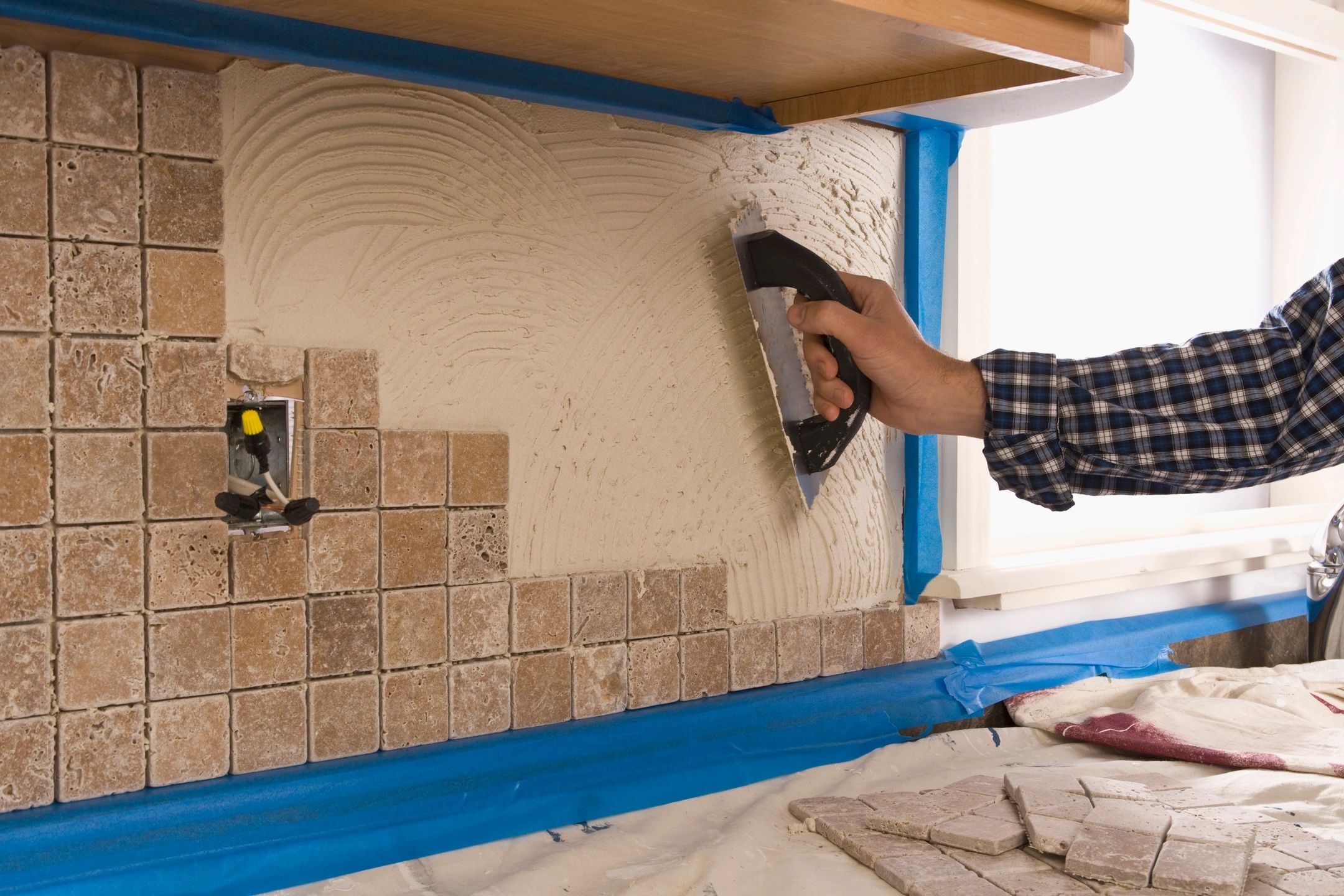 Person smoothing adhesive on wall tiles during installation.