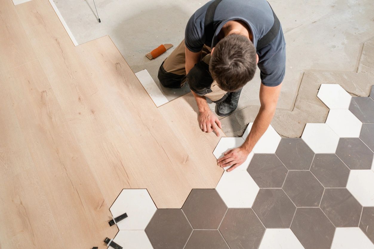 Person installing hexagonal tiles next to wooden flooring.